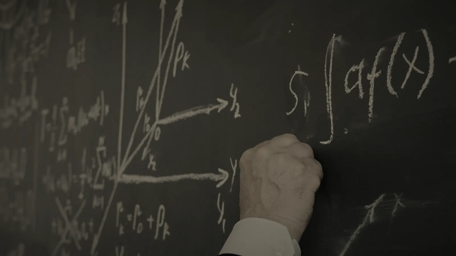 A hand writing mathematical formulas in chalk on a blackboard