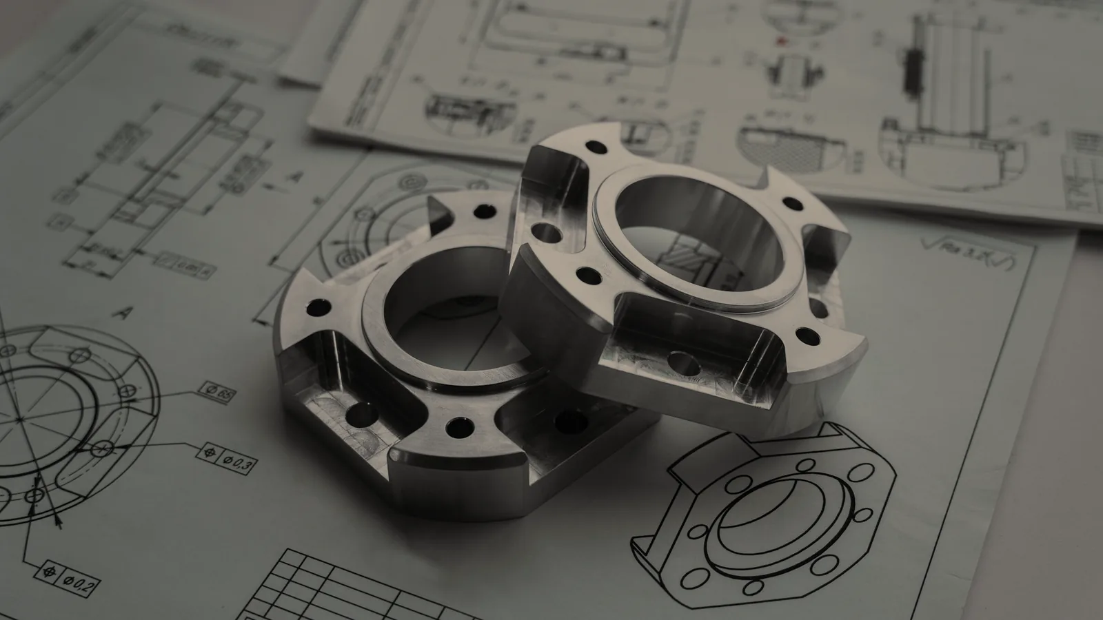Two machined metal parts resting on the engineering drawings they were built from