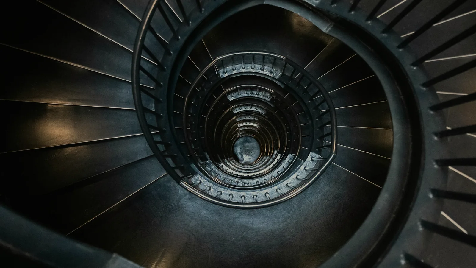 A dark spiral staircase seen from above, each flight coiling into the one below